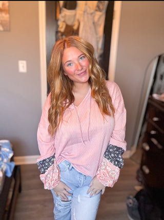 Woman wearing a pink blouse with lace cuffs in a casual indoor setting