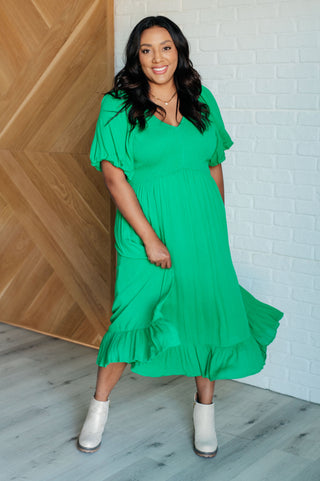 Woman wearing a green dress standing against a white brick wall.
