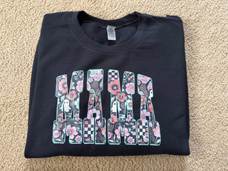Folded black t-shirt with floral lettering on a beige carpet