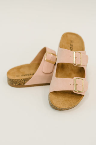 Pair of pink sandals with gold buckles on a light background