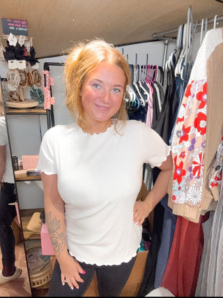 Woman in a white shirt standing in a clothing store with racks of clothes in the background.