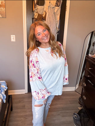 Woman wearing a light blue floral top and ripped jeans in a room with a dresser and mirror.