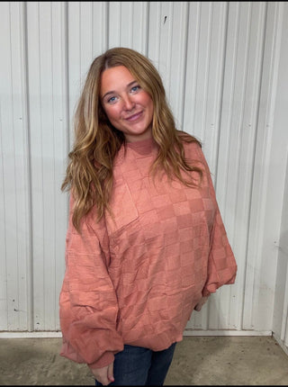 Woman wearing a pink oversized sweater in front of a white paneled wall.